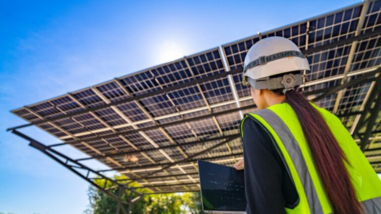 Solar technician inspects a panel with a tablet. The screen visualizes what the SCADA system is, the solar park's digital control.