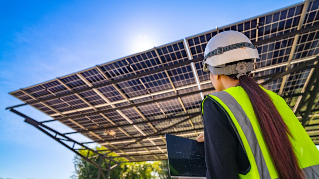 Solar technician inspects a panel with a tablet. The screen visualizes what the SCADA system is, the solar park's digital control.